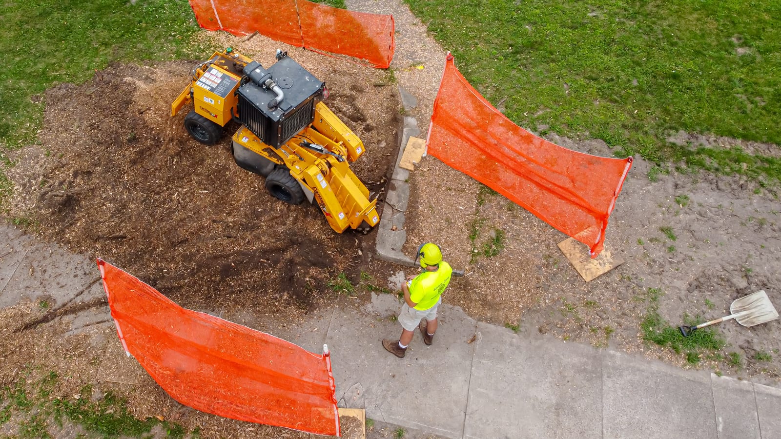 Overhead view of a self-propelled stump grinder clearing a tree stump beside a walkway (stock photo; not a completed local project photo)